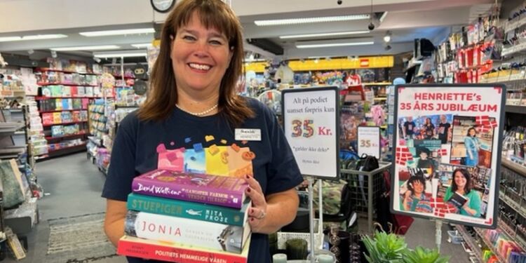Henriette med en står stak bøger, som udloddes i forbindelse med jubilæet hos Bog & idé i Hirtshals.