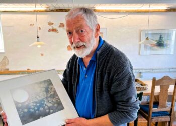 Christian Hansen med et af de billeder, der viser en mere abstrakt side af hans univers end de karakteristiske billeder med motiver fra naturen i og omkring Hirtshals. I baggrunden til højre et af dem, som de fleste relaterer til Christian Hansen og Hirtshals. Foto (arkiv): Niels Skipper.
