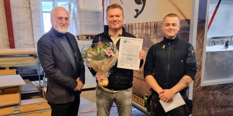 Direktør Neil Jacobsen fra EUC Nord overrakte blomster og diplom til direktør Henrik Fjordbak og lille gave til tømrerlærling Sebastian Dahl Sørensen. Foto: EUC Nord.
