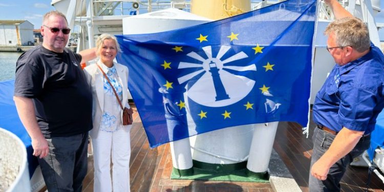 Formand Peter Jensen fra Støtteforeningen Hirtshals Fyr, turistchef Laila Zielke og direktør Espen Frøysland fra Lindesnes Fyrmuseum holder flaget med logoet for European Route of Lighthouses. Foto: Niels Skipper.